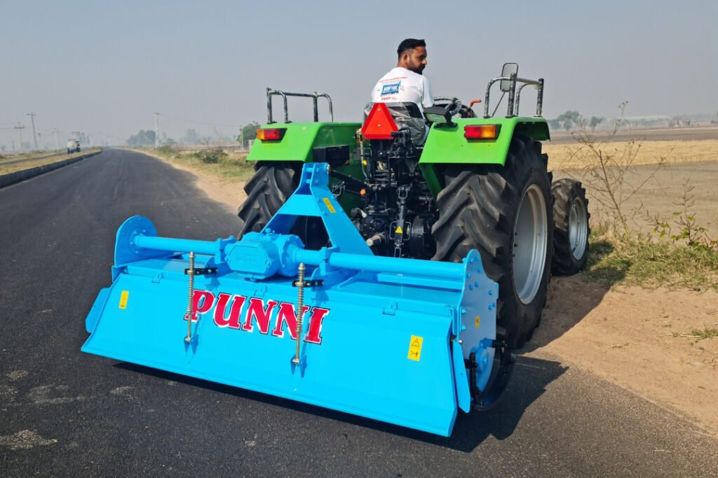 rotavator | A closeup view of the back side of a sky blue PUNNI Rotavator attached to a tractor in a field